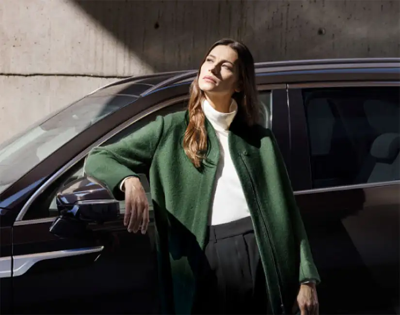 Lady in green coat leaning up against a Kia