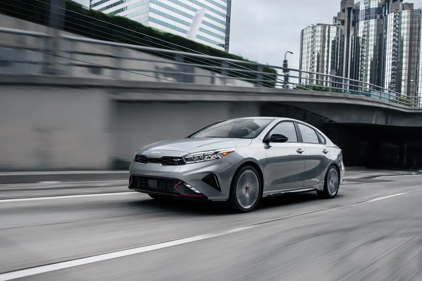 2023 Kia Forte used as a compact fleet vehicle driving down a highway in a city downtown.